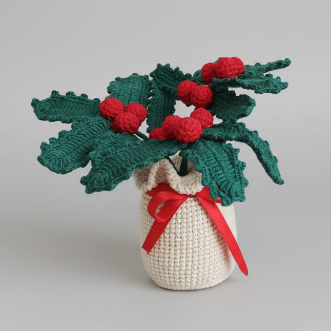 Crocheted potted orchid amigurumi with green leaves, red buds, and red bow on white pot