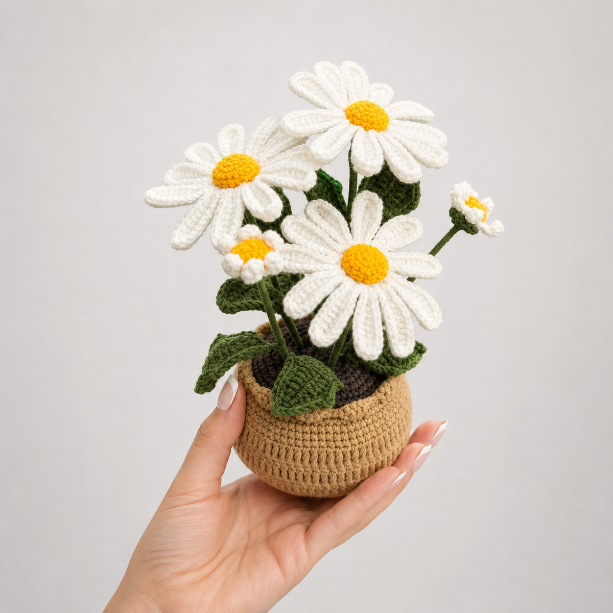 Handmade crochet daisy flowers in beige crocheted vase, held in hand