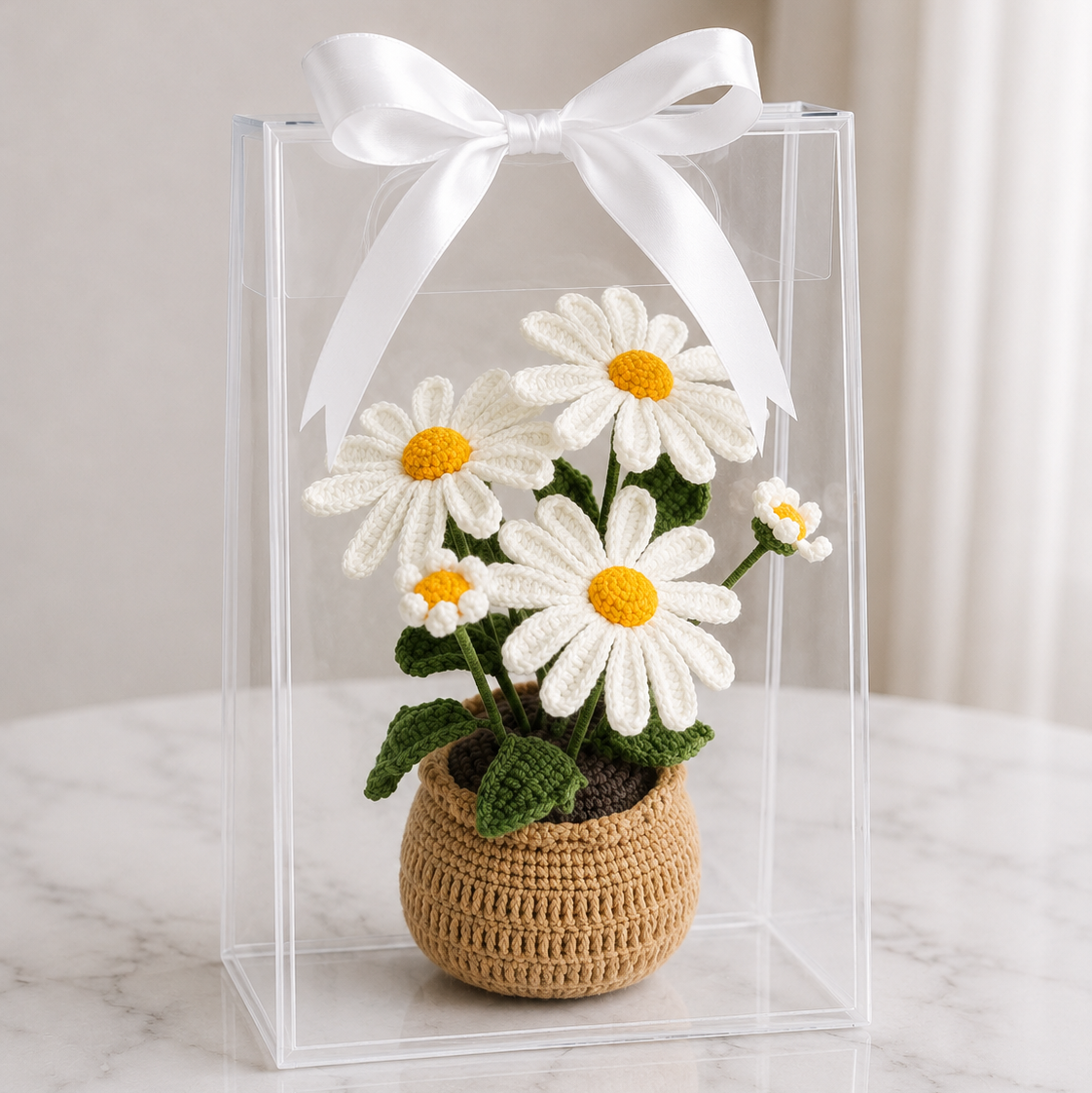 Crochet daisy arrangement in beige vase inside clear acrylic box with white ribbon