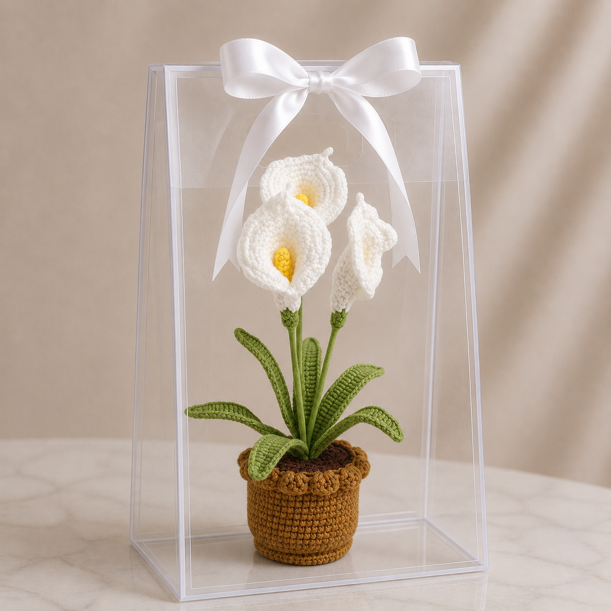 Crocheted white lily plant in brown pot with green leaves, inside clear gift box