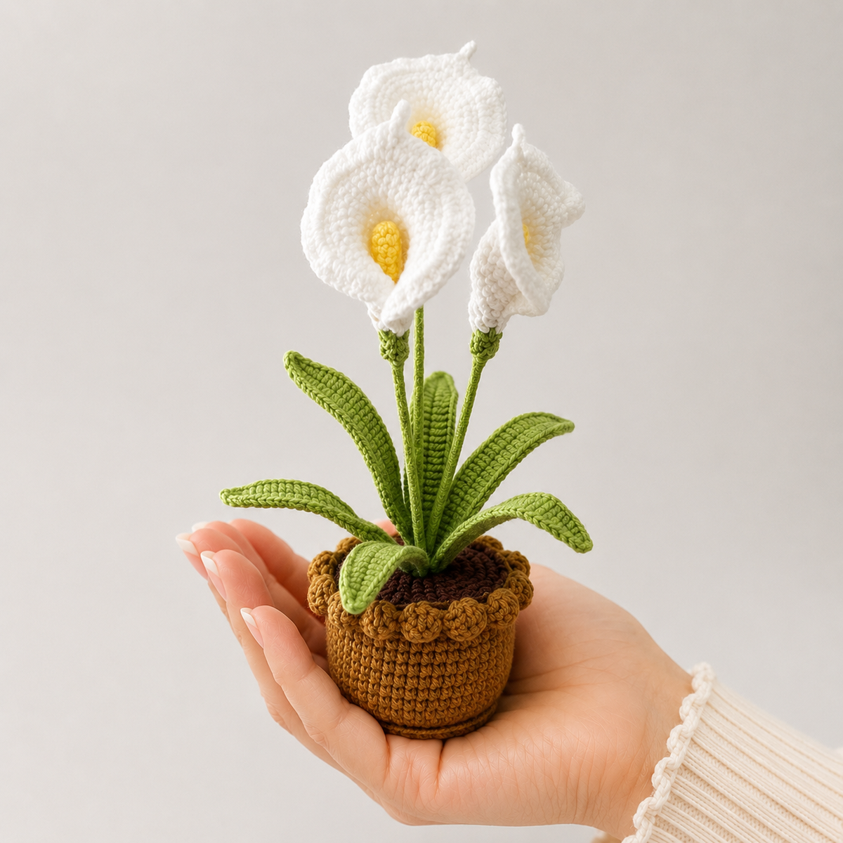 Crocheted white lily plant with green leaves in brown pot held in hand