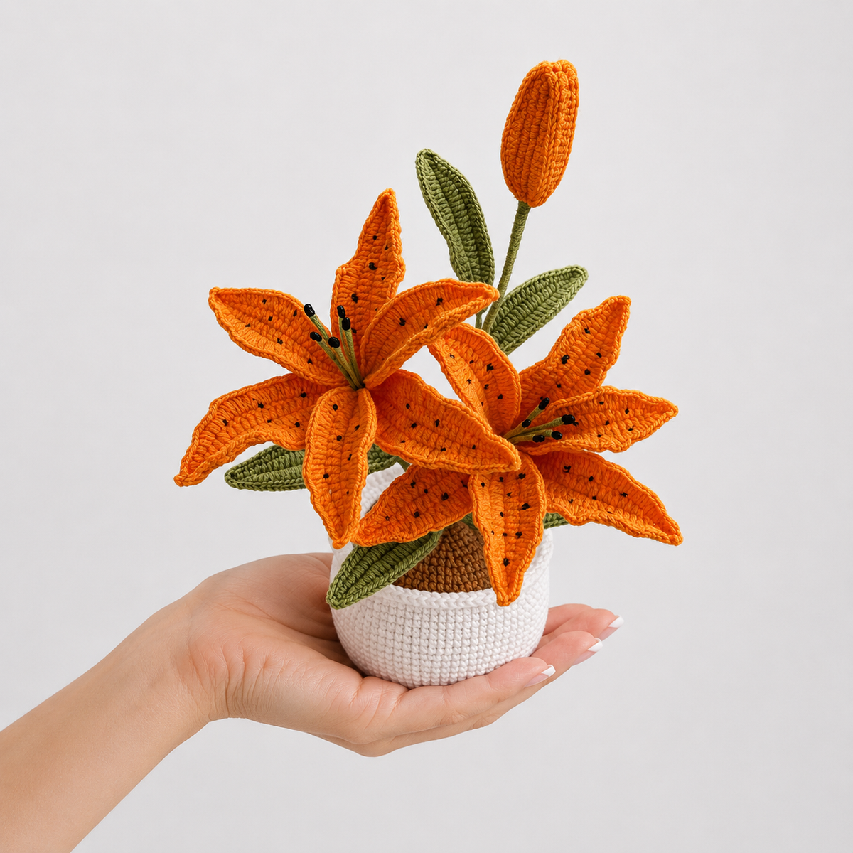 Handmade crochet orange lily in white textured pot, held in a hand