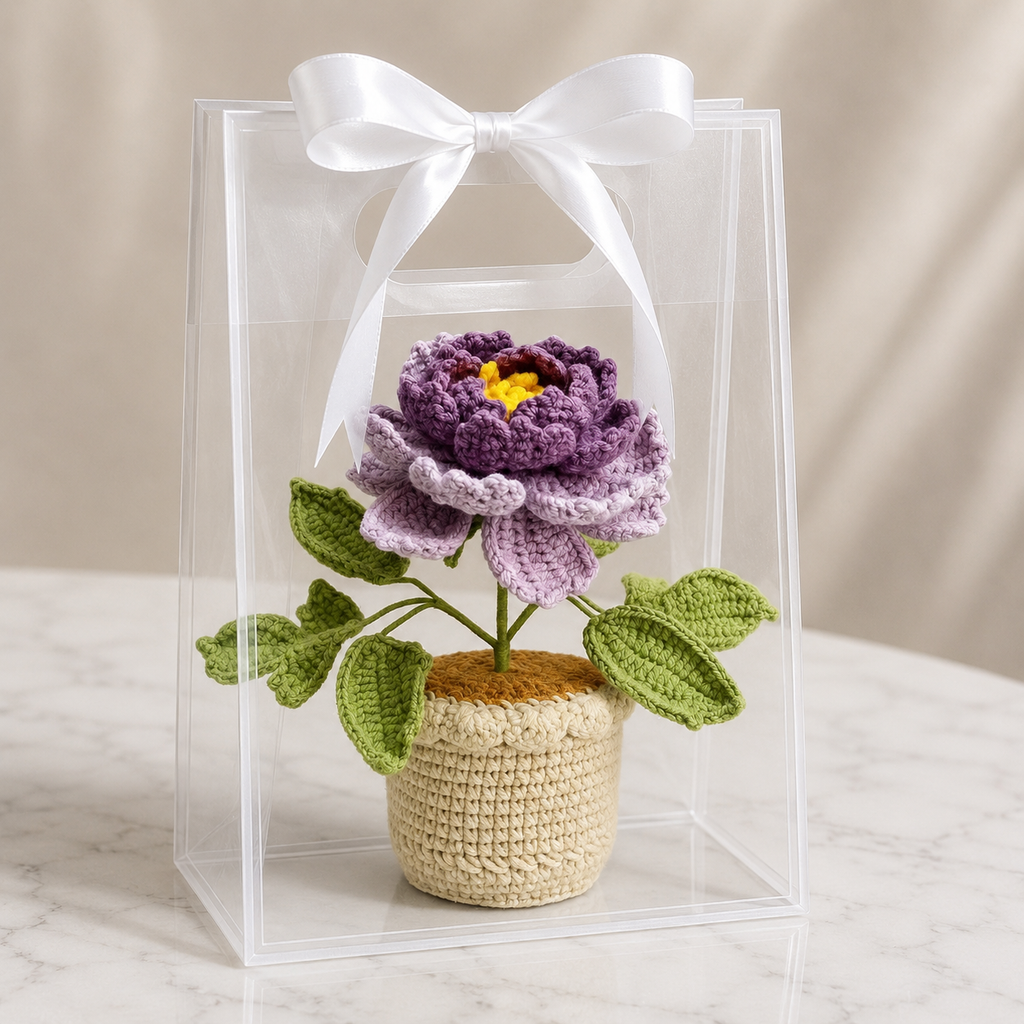 Handmade crochet peony in beige pot with white ribbon bow, purple flower and green leaves