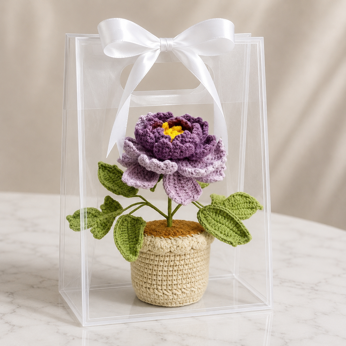 Handmade crochet peony in beige pot with white ribbon bow, purple flower and green leaves