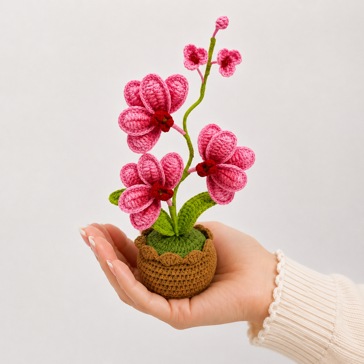 Crochet orchid with pink blossoms in brown pot held in a person's hand