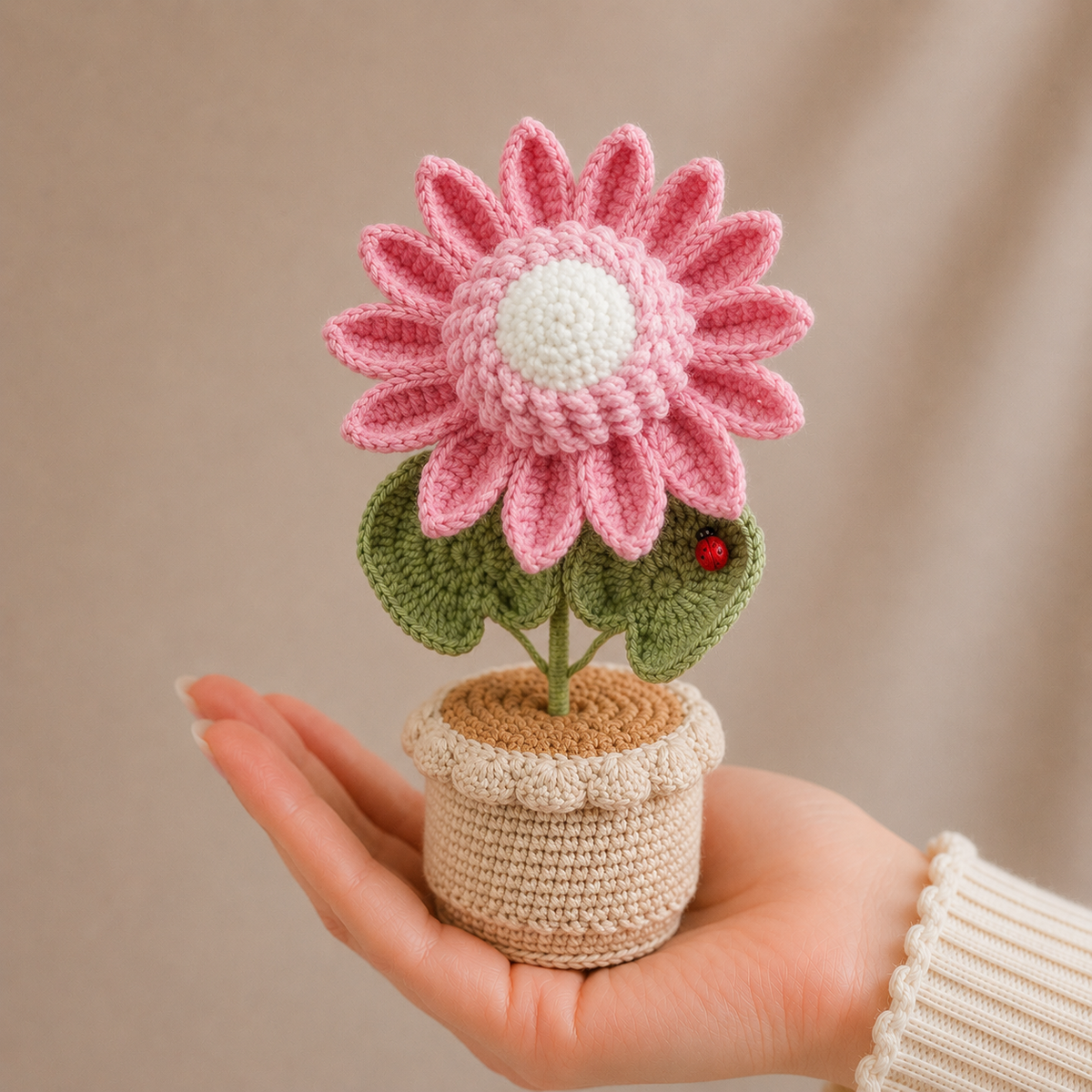 Handmade crochet sunflower in pot held in hand, pink petals, green leaves
