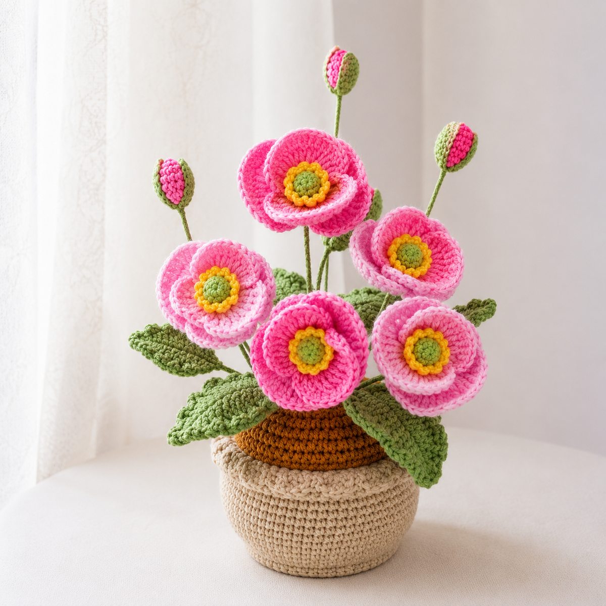 Crocheted pink poppies in beige yarn pot with green leaves
