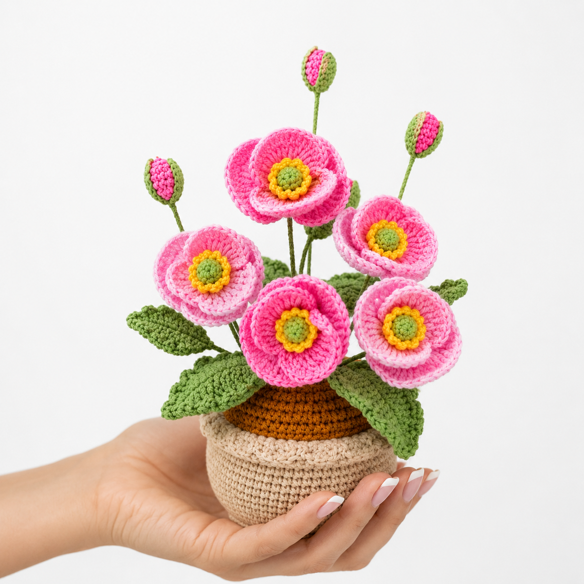Handheld crocheted pink poppies in beige yarn pot with green leaves