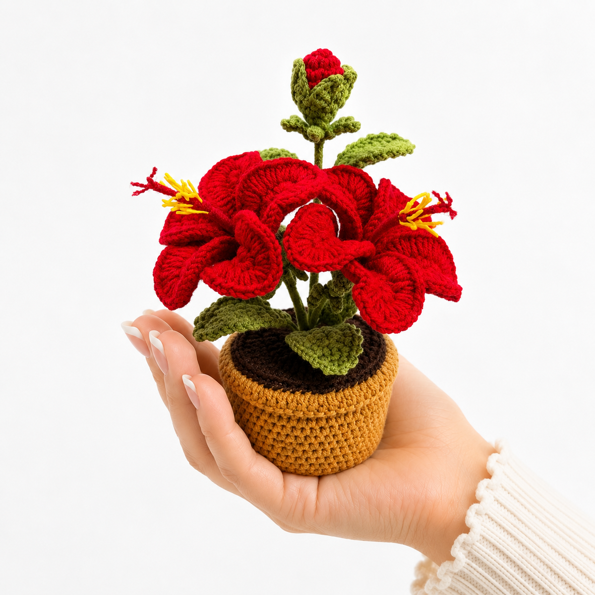 Crocheted red lily amigurumi flower in tan pot with green leaves, held in a hand.