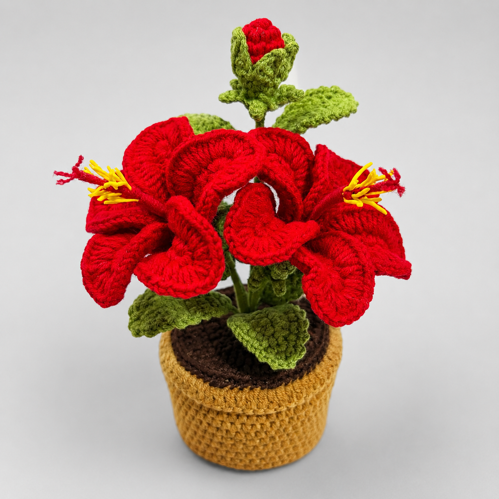 Crocheted red lily amigurumi flower in tan pot with green leaves and stems.