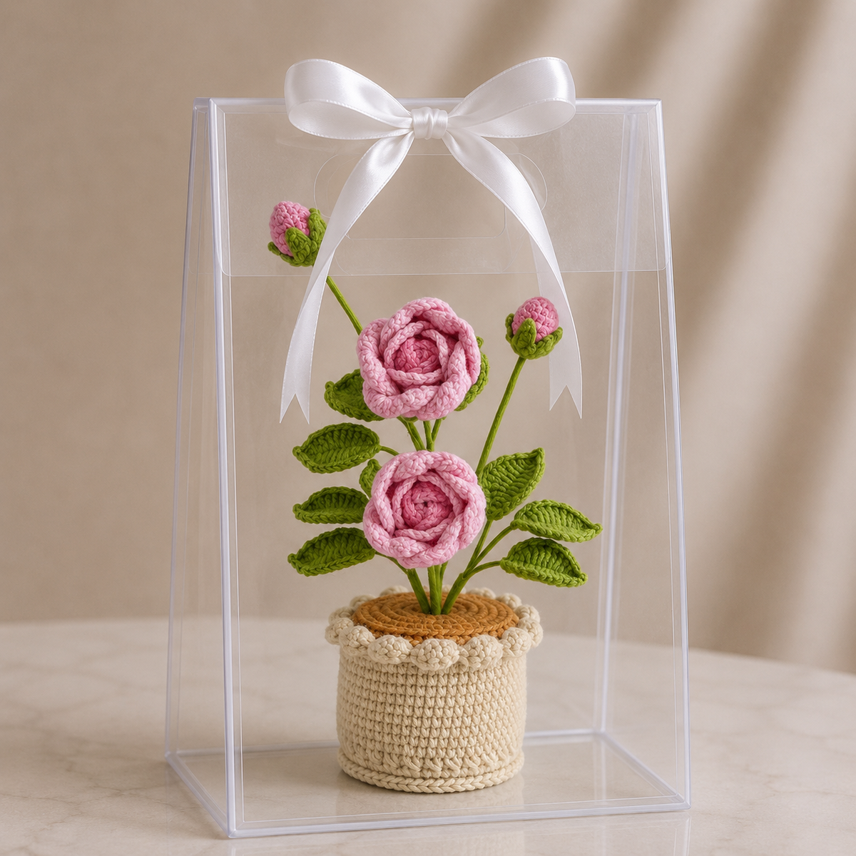 Crochet rose flower in beige pot with pink blooms, in clear gift box with white bow