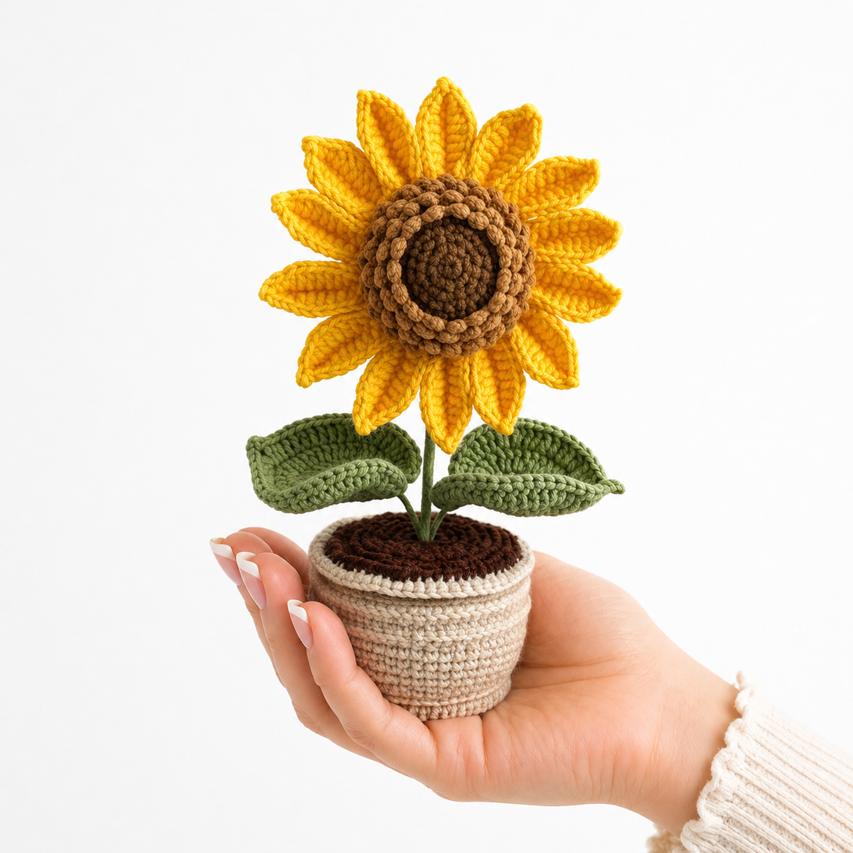 Handmade crocheted sunflower plant in a crocheted pot with green leaves, held in hand.