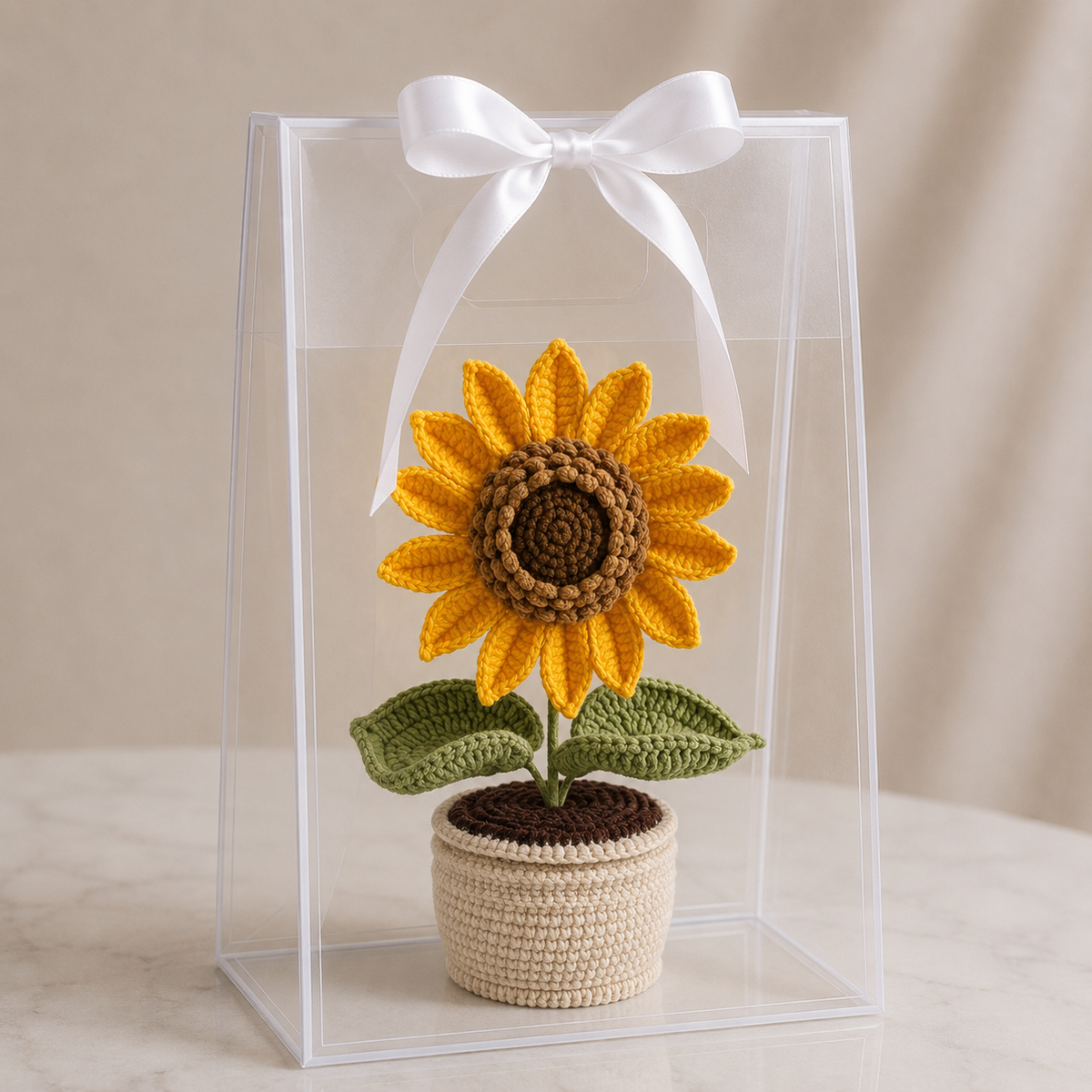 Crochet sunflower potted plant in clear gift box with white bow ribbon.