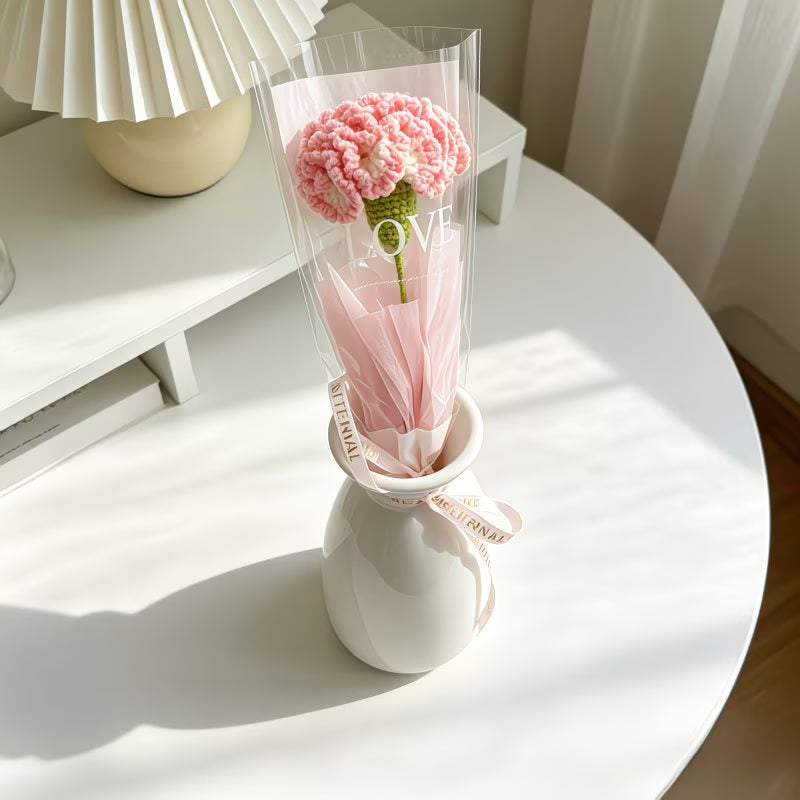 Crocheted pink carnation single-stem bouquet in clear wrap with pink ribbon