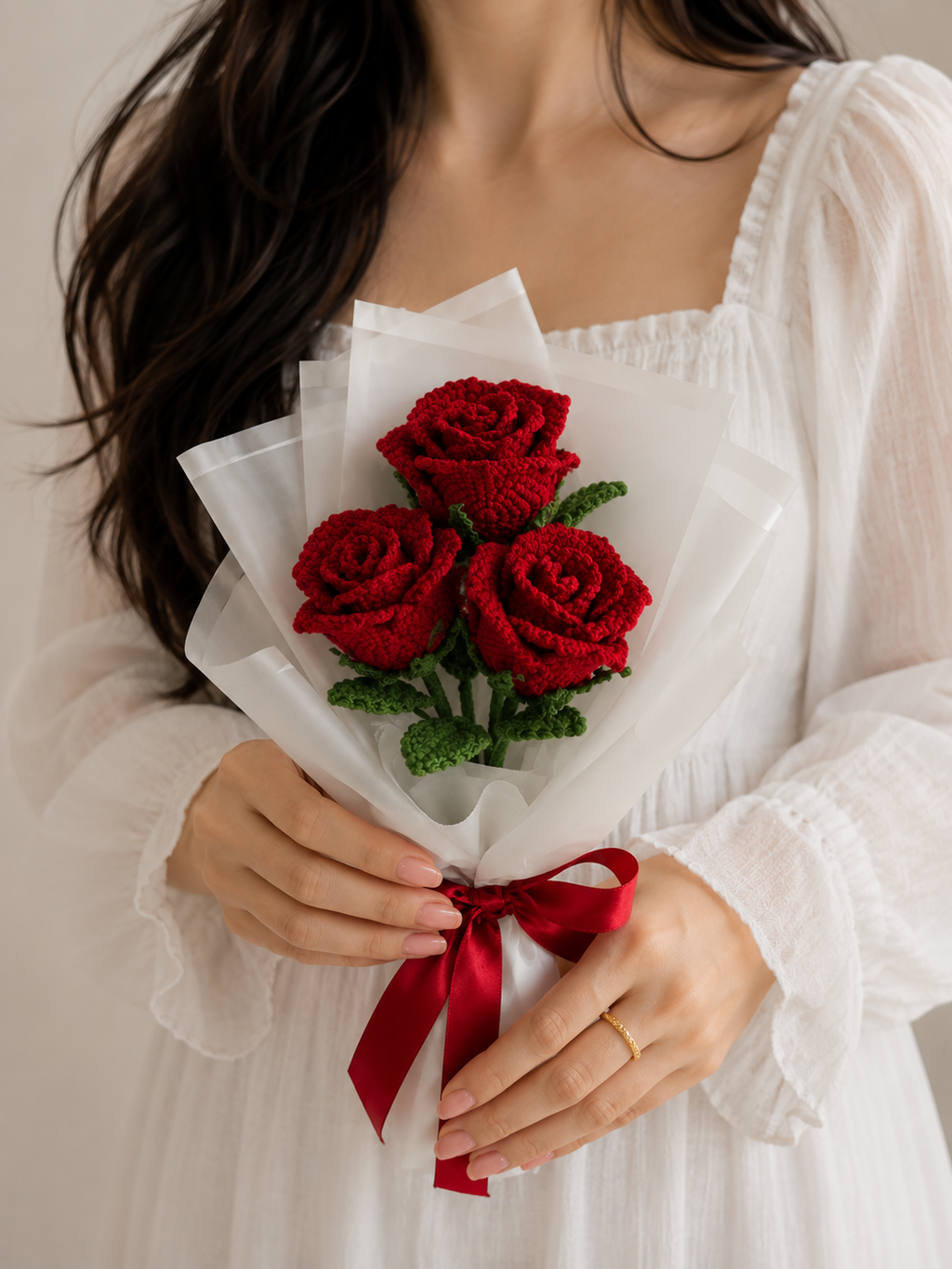 Handmade crocheted rose bouquet with three red blooms, green leaves, white wrap and red ribbon