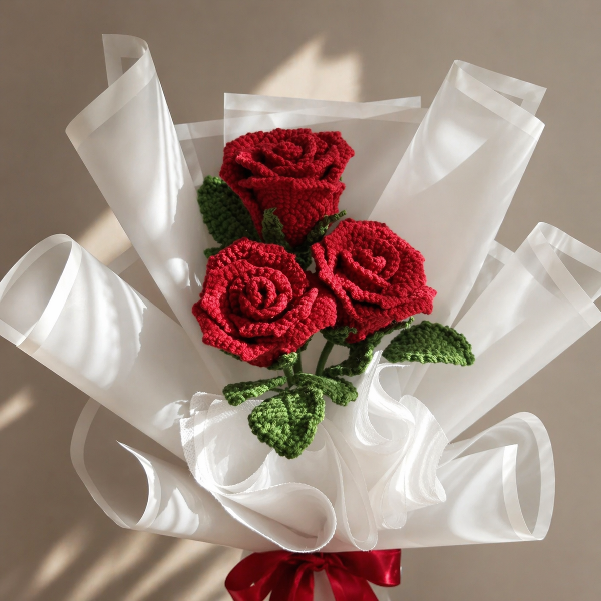 Handmade crocheted rose bouquet with red flowers, green leaves, white wrap, red satin bow