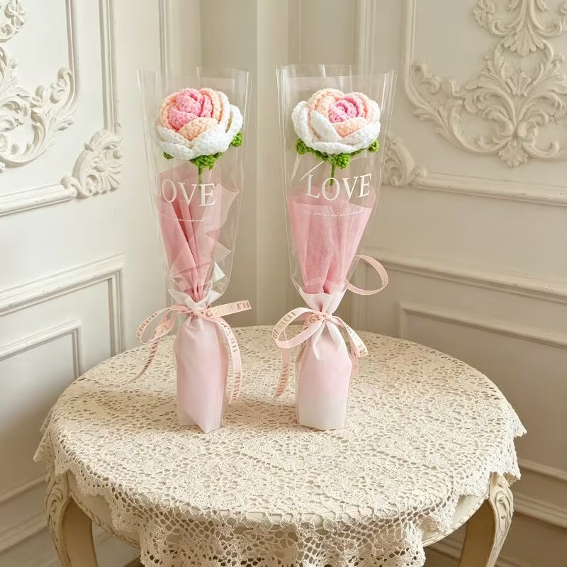 Two pink crocheted rose single-stem bouquets in sheer sleeves with ribbon ties